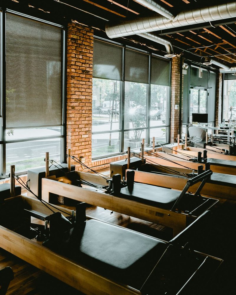 A boutique Pilates studio with wood reformers, brick walls, and warm window light